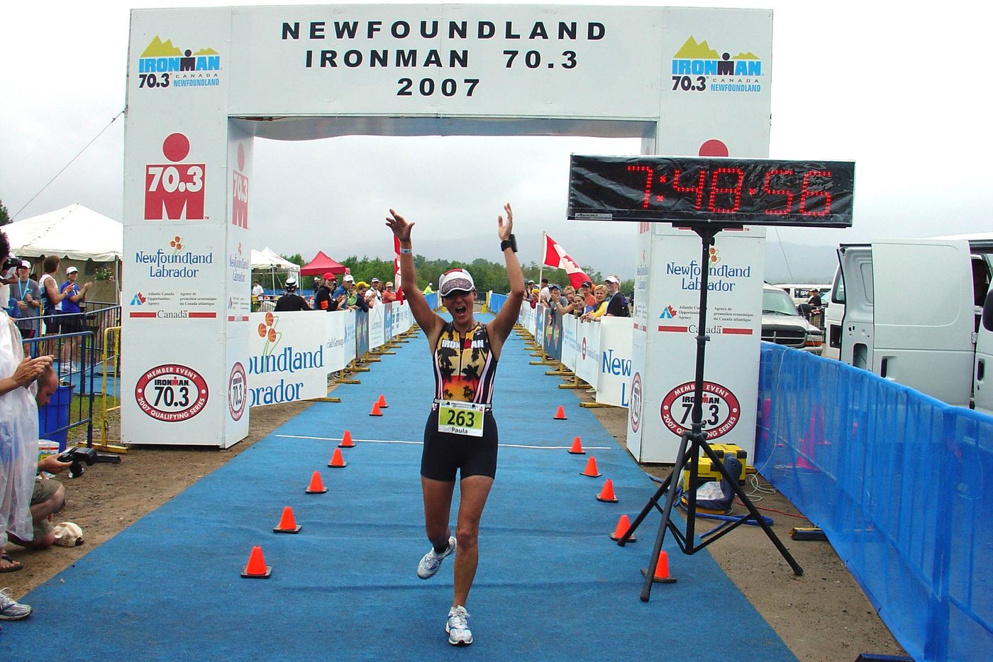 Paula crossing the Newfoundland Ironman 70.3 finish line in 2007, arms raised high, mid-shout of joy.